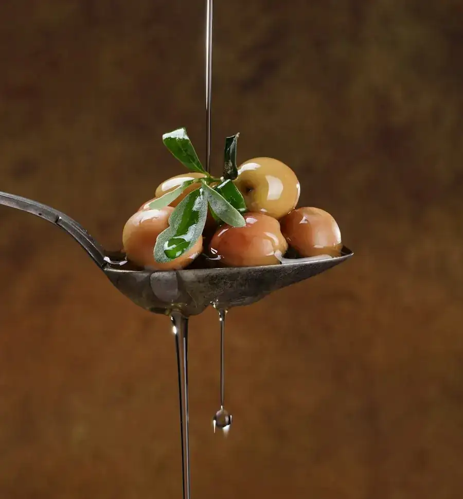 Green olives on a metal spoon against a warm brown background