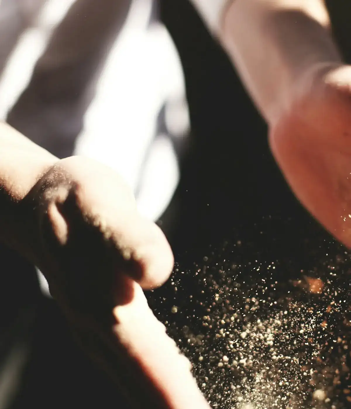 Hands scattering ground spice through a shaft of light